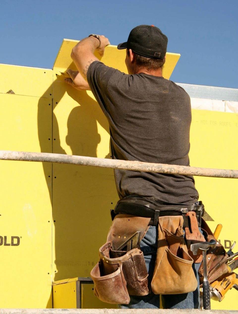 A man in brown pants and hat painting a wall.